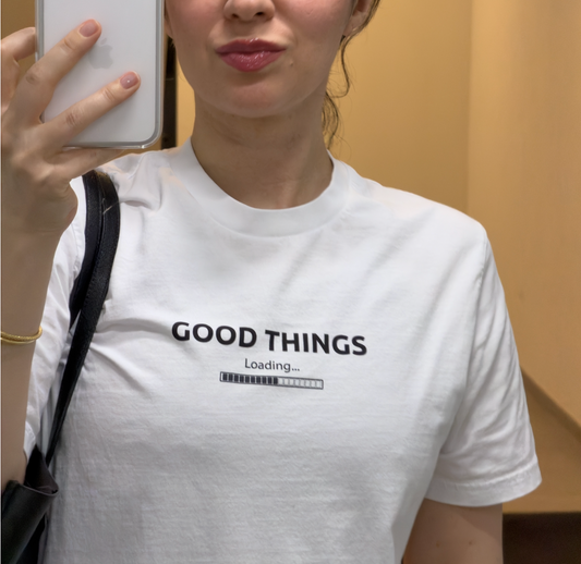 Woman wearing a white organic cotton graphic tee with "Good Things Loading" print, minimal and relaxed style — Island of Calm