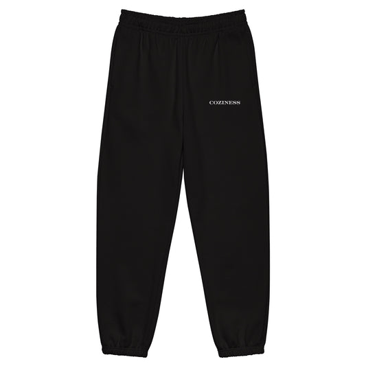 Heavyweight sweatpants in Black with soft brushed fleece, white “coziness” embroidery, deep side pockets, elastic cuffs, and relaxed street-style fit.